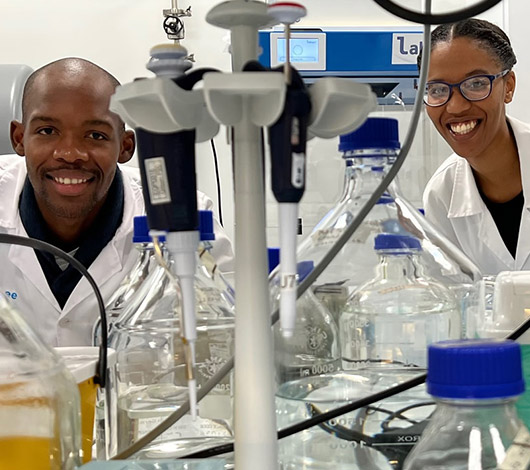 two Afrigen Biologics scientists in lab looking at camera